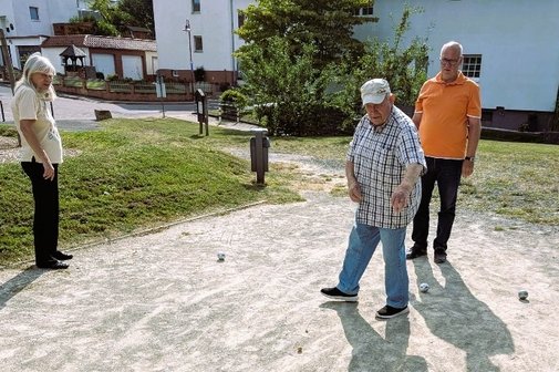 Spieler beim Boulen Hier sieht man zwei Männer und eine Frau auf dem Bouleplatz, mit ein paar Boulekugeln auf dem Boden liegend.