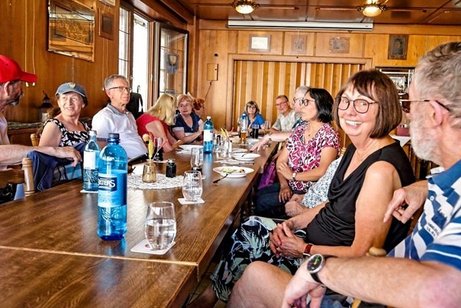 Ein Abend ganz nach dem Motto &bdquo;Zusammensitzen, babbeln und eine sch&ouml;ne Zeit miteinander verbringen&ldquo;: An einer langen, rustikalen Tisch sitzen die G&auml;ste in gem&uuml;tlicher Runde beisammen. Bei einem k&uuml;hlen Getr&auml;nk, gutem Essen und vielen angeregten Gespr&auml;chen wird gelacht, erz&auml;hlt und gemeinsam der Abend genossen. Die warme Holztische und die entspannte Atmosph&auml;re machen das Bild besonders heimelig. Ein geselliger Babbel-Abend mit viel guter Laune, netten Menschen und jeder Menge Gespr&auml;chsstoff.