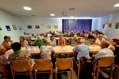 ein Saal mit 3 Tischreihen an den Personen sitzen, die sich unterhalten.