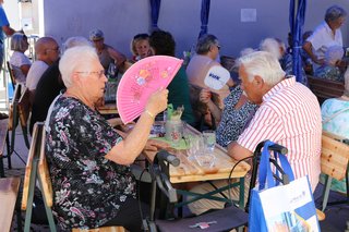 Besucher an den Tischen beim Grillfest fächeln sich mit einem Fächer Luft zu