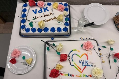 Torten von vorne Fotografiert. Auf der Torte ist das Herz in Regenbogenfarben und mit buntem Schriftzug: "Menschen mit Herz". Dazu verteilt Zuckerrosen.