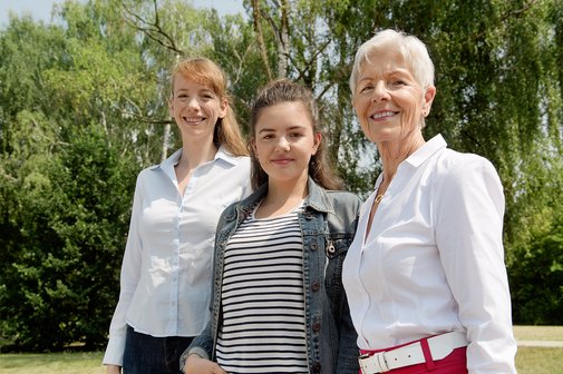 Drei Frauen l&auml;cheln gemeinsam in die Kamera: Eine j&uuml;ngere, eine Teenagerin und eine &auml;ltere Frau.
