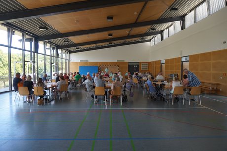 Übersicht der Bestuhlung mit anwesenden Mitgliedern während der Vorsitzende, im Hintergrund, die Versammlung eröffnet.