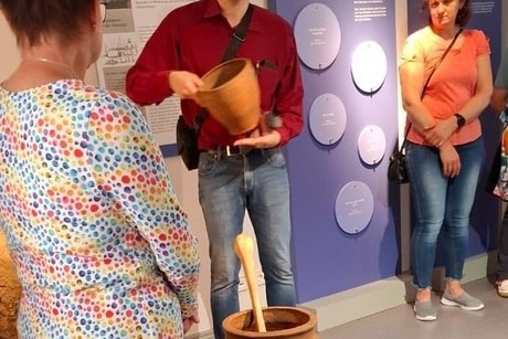 In der Mildmitte steht der Museumsleiter und erklärt. 2 Frauen stehen daneben.