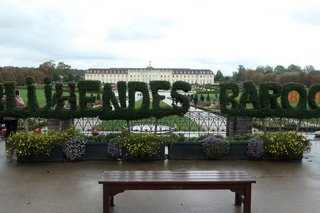 Eingang vom Schloss. Eine Hecke bildet die Worte "BLÜHENDES BAROCK". In Hintergrund ist das Schloss.