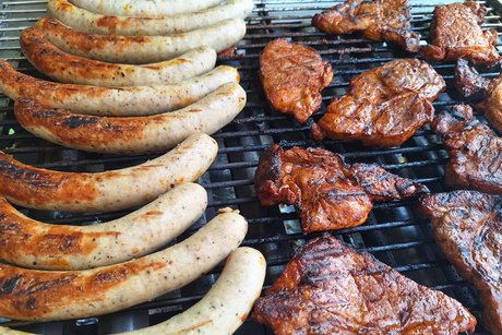 Ein Grillrost mit Bratw&uuml;rsten und Steaks. Die W&uuml;rste brauchen noch ein wenig Br&auml;une.