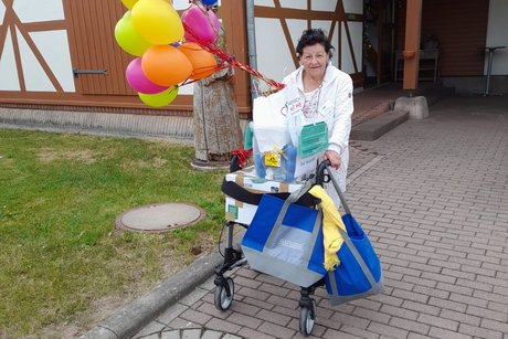 Eine Frau fährt mit einem Rollator, an dem viele Luftballons hängen.