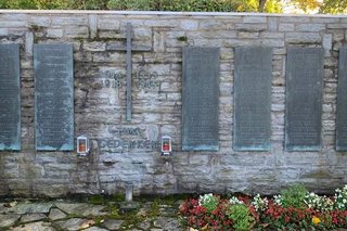 Das Bild zeigt das Mahnmal auf dem Schwalbacher Friedhof mit, die Namen der Gefallenen und Vermissten des 1. und 2. Weltkrieges aus Schwalbach. Zwei Kerzen und Blumen runden das Bild ab.