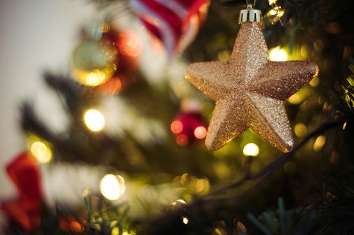 Anh&auml;nger eines Goldenen Sterns h&auml;ngt an einem dekorierten und beleuchteten Weihnachtsbaum