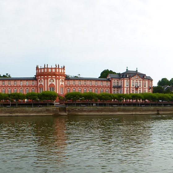 Gebäudeansicht Biebricher Schloss, fotografiert von einem Schiff auf dem Rhein aus , im Vordergrund sieht man den Rhein und die Uferpromenade.