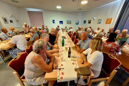 Ein kleinerer Saal mit ca. 50 Menschen an 3 Tischreihen