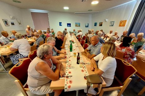 Ein kleinerer Saal mit ca. 50 Menschen an 3 Tischreihen