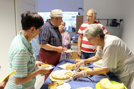 Besucherinnen und Besucher des Kaffeenachmittags suchen sich am Kuchenbuffet Kuchen aus.