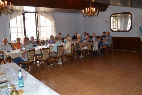 Die Anwesenden (Saal, links) hören den Bericht der Vorsitzenden.