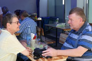 Zwei Besucher des Grillnachmittags sitzen an einem Biertisch und unterhalten sich.