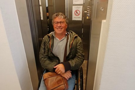 Das Bild zeigt Hermann Roth vor dem Aufzug, der zu klein ist f&uuml;r den Rollstuhl.