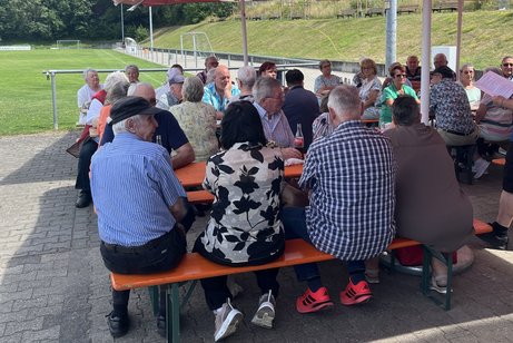 Personen auf Bierzeltgarnituren in Gespr&auml;chen