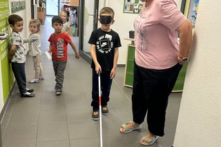 Das Bild zeigt Anette Leissner, die die Kinder mit Blindenstock sicher durch die KITA