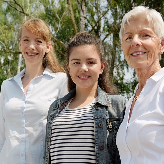 Drei Frauen l&auml;cheln gemeinsam in die Kamera: Eine j&uuml;ngere, eine Teenagerin und eine &auml;ltere Frau.
