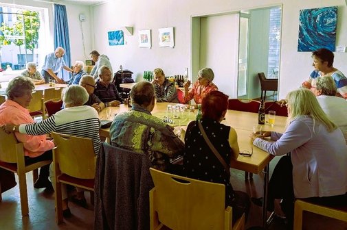 Gesellige Zeit in der Begegnungsstätte Ein Raum mit mehreren Tischen an denen eine Vielzahl von meist älteren Menschen sitzen, sie haben Getränke auf den Tischen stehen und unterhalten sich.