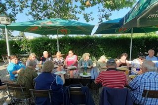 Das Bild zeigt 16 Personen an einem Tisch im Biergraten