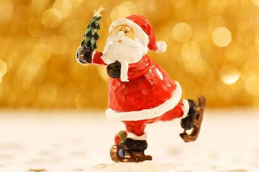 Eine kleine bemalte Figur eines Weihnachtsmannes. Er läuft auf Schlittschuhen und hält einen kleinen Weihnachtsbaum in der Hand.