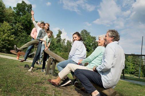 Junge und alte Menschen und ein Kind sitzen auf einer Wippe auf einem Spielplatz