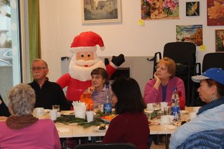 Um einen weihnachtlich gedeckten Tisch sitzen 10 Parsonen. Dahinter winkt ein aufgeblasener Weihnachtsmann.