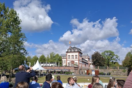 Unter einem blauen Himmel mit wei&szlig;en Wolken ist das Schloss zu sehen. Im Vordergrund ist das Oberdeck mit vielen Fahrg&auml;sten.