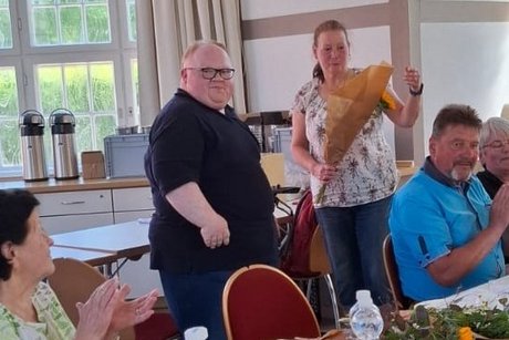 G&auml;ste am Tisch und im Hintergrund wird ein Blumenstrau&szlig; &uuml;bergeben.