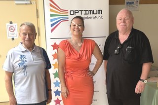 Auf dem Foto sehen Sie von links Willi Beck, Verena Campbell und Helmut Müller vor dem Roll-Up OPTIMUM Pflegeberatung