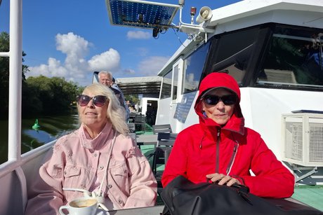 Zwei &auml;ltere Damen mit Sonnenbrille sitzen in der Sonne auf dem Deck an einem Tisch.