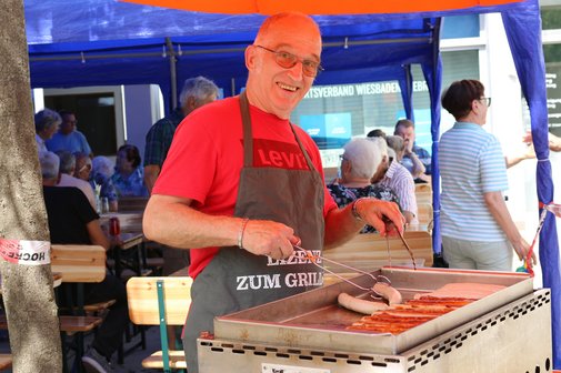 Ein Vorstandsmitglied grillt am Grillstand Würstchen und Steaks.
