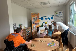 Das Bild zeigt im Hintergrund Kinder bei der Fühlstation um gleiche Karten zu erfühlen.