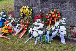 Verschiedene Gestecke und Gebinde liegen vor dem Denkmal.