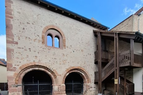 Ein Steinhaus mit zwei gro&szlig;en Torb&ouml;gen vorne. Rechts f&uuml;hrt eine h&ouml;lzerne Freitreppe in den ersten Stock.