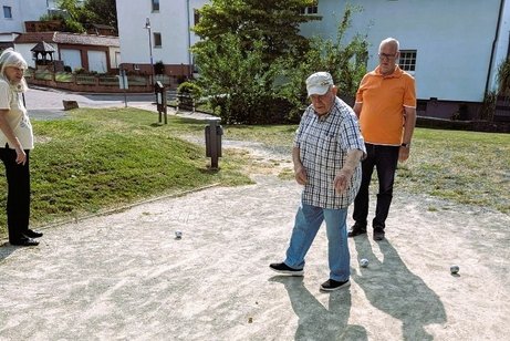 Hier sieht man zwei M&auml;nner und eine Frau auf dem Bouleplatz, mit ein paar Boulekugeln auf dem Boden liegend.