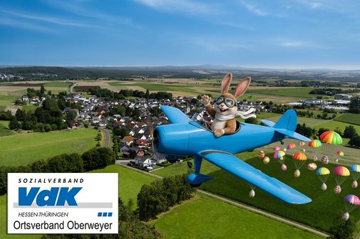 Auf dem Bild ist ein lustiger Osterhase in einem Flugzeug &uuml;ber dem Ort Oberweyer zu sehen. Aus dem Flugzeug fallen bunte Ostereier an Fallschirmen herunter.