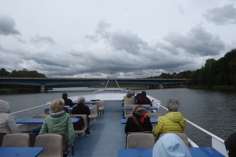 Mitglieder sitzen auf einem Schiff auf dem oberen Deck - Blick über die Seenplatte von Bord