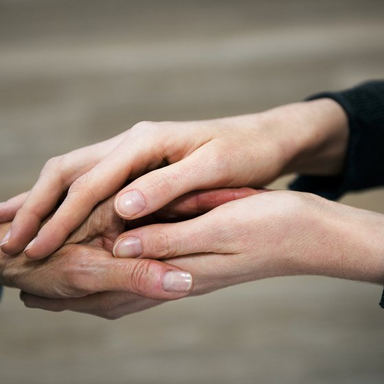 Die Hand einer j&uuml;ngeren Frau h&auml;lt die Hand einer &auml;lteren Frau in einer tr&ouml;stenden Geste.