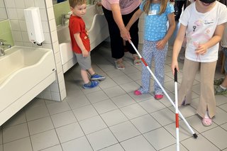 Das Bild zeigt Anette Leissner, die die Kinder mit Blindenstock sicher durch die Sanitäranlage