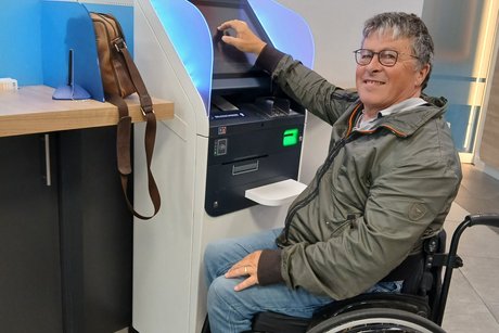 Das Bild zeigt Hermann Roth im Rollstuhl sitzend vor dem Kontoauszugsdrucker