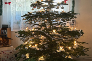 Das Bild zeigt einen Geschmückten Weihnachtsbaum mit Silbernen Weihnachtskugeln, leuchtende Kerzen und weiterem Baumschmuck