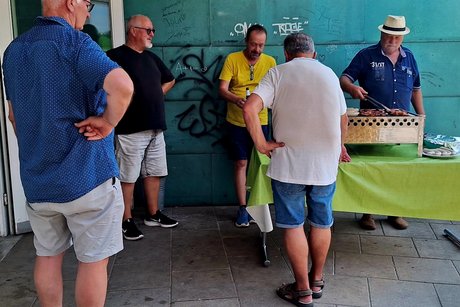 F&uuml;nf M&auml;nner stehen um den Grill, w&auml;hrend einer der M&auml;nner das Fleisch wendet