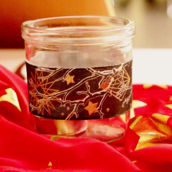 Kerzenglas auf weihnachtlich mit Sternen dekorierter roter Tischdecke