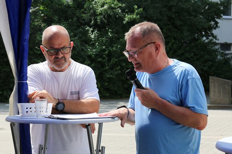 Der stellvertretende Ortsverbands-Vorsitzende Michael Koshold-Gerich steht rechts an einem Stehtisch, hat ein Mikrofon in der Hand und begrüßt die Gäste. Links im Bild Jimmy Cela, Kassierer im Biebricher VdK-Ortsverband.