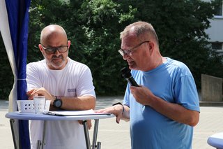 Der stellvertretende Ortsverbands-Vorsitzende Michael Koshold-Gerich steht rechts an einem Stehtisch, hat ein Mikrofon in der Hand und begrüßt die Gäste. Links im Bild Jimmy Cela, Kassierer im Biebricher VdK-Ortsverband.