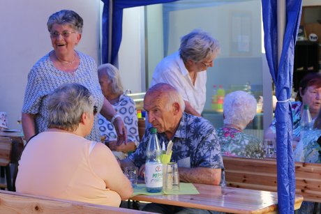 Besucher des Grillfests sitzen an Tischen