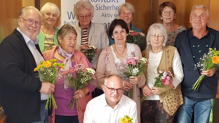 10 Personen mit Blumensträußen in den Händen stehen im Gruppenbild zusammen.