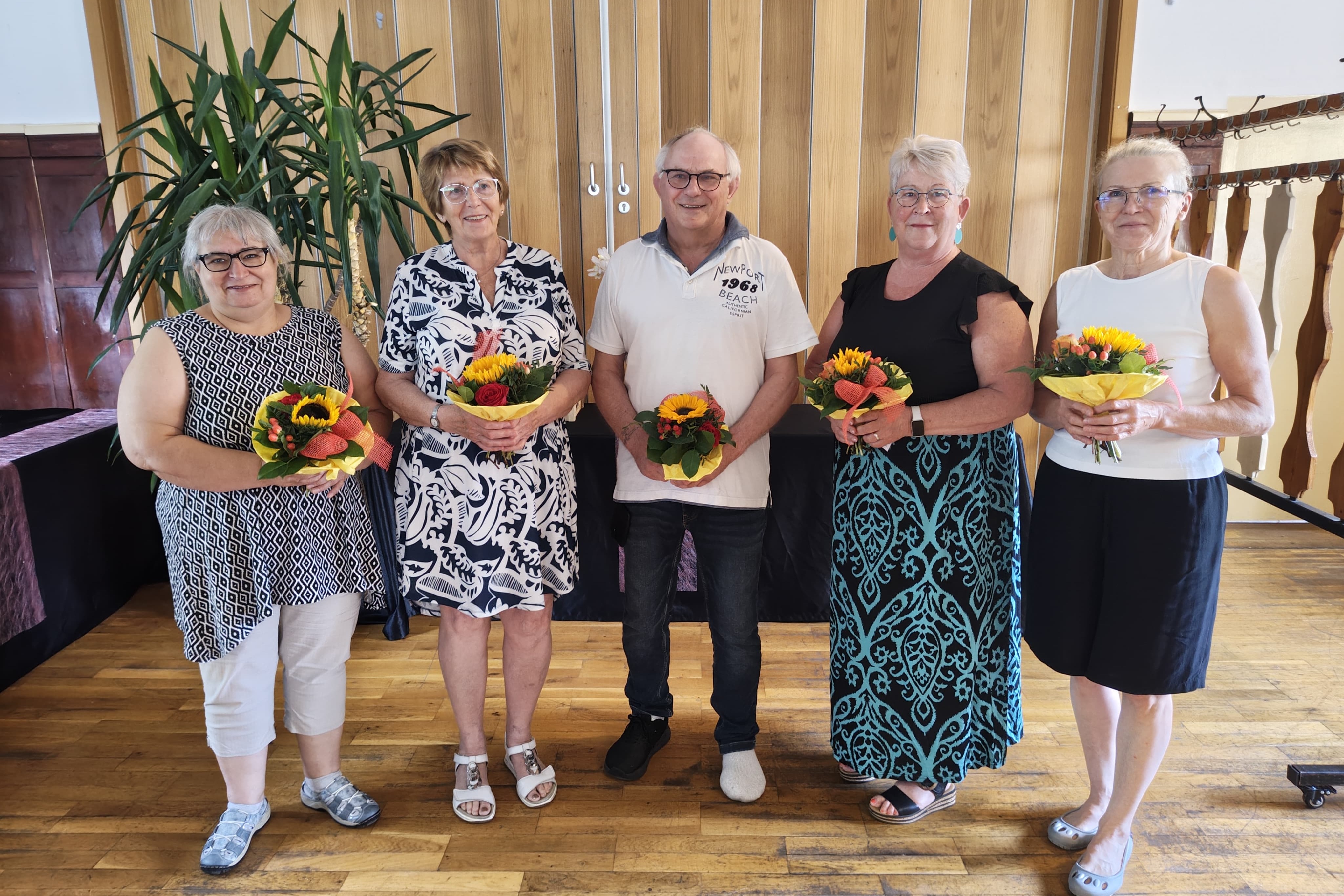 5 Personen mit Blumenstr&auml;u&szlig;en in den H&auml;nden stehen im Gruppenbild zusammen.